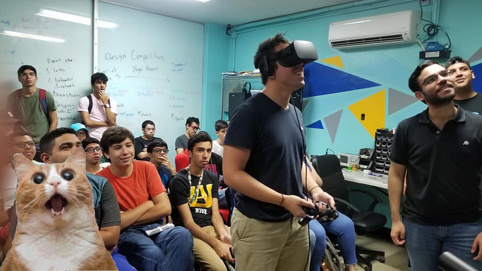 A Visionary member demos a VR headset to a packed room during a hackathon at UPR Mayagüez